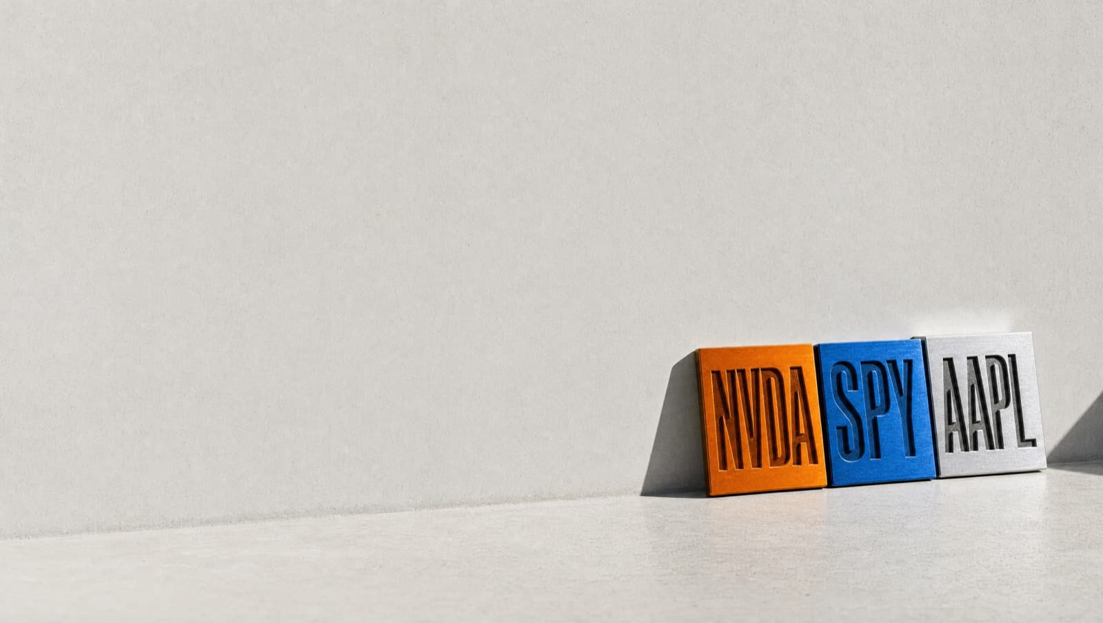 Three anodised metal plates engraved NVDA, SPY and AAPL, leaning against a concrete wall in hard sunlight